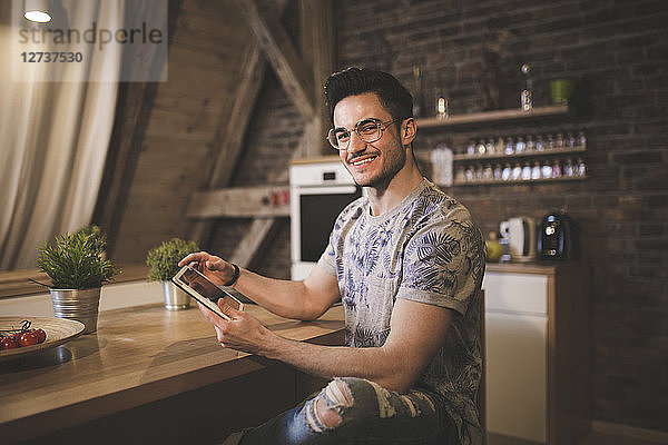 Portrait of smiling young man using tablet in kitchen at home