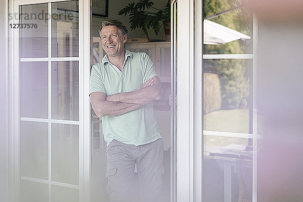 Laughing mature man standing at French window