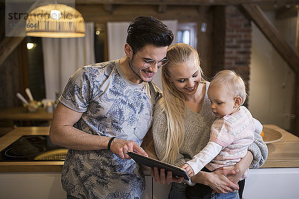 Happy young parents using tablet at home with their baby girl