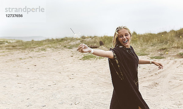 Spain  Aviles  happy teenage girl holding a sparkler on the beach