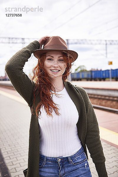Portrait of smiling redheaded woman with brown hat at platform
