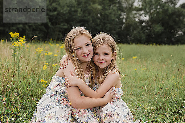 Two little sisters hugging each other on a meadow