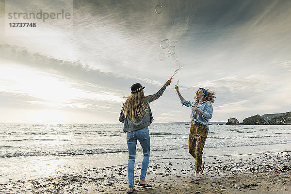 Happy friends making soap bubbles on the beach