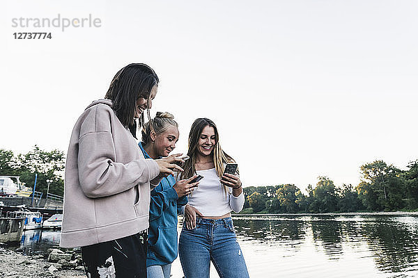 Three young women using cell phones at the riverside