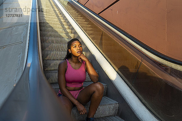 Young sportive woman sitting on escalator