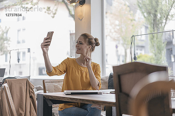 Young woman sitting in coworking space  taking smartphone selfie