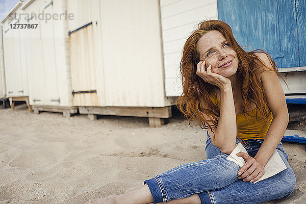 Redheaded woman sitting in front of beach cabin  reading a book