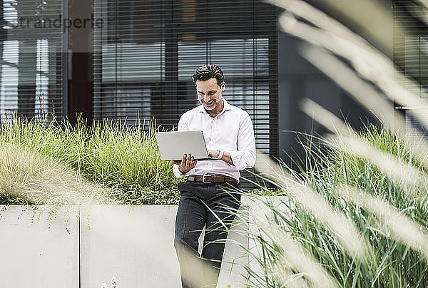 Smiling businessman using laptop outside office building