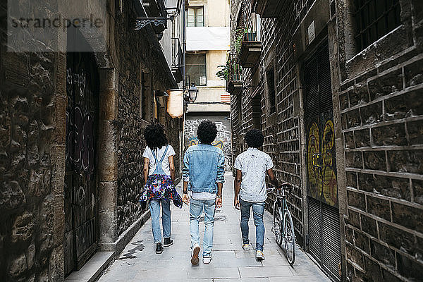 Spain  Barcelona  back view of three friends walking down an alley