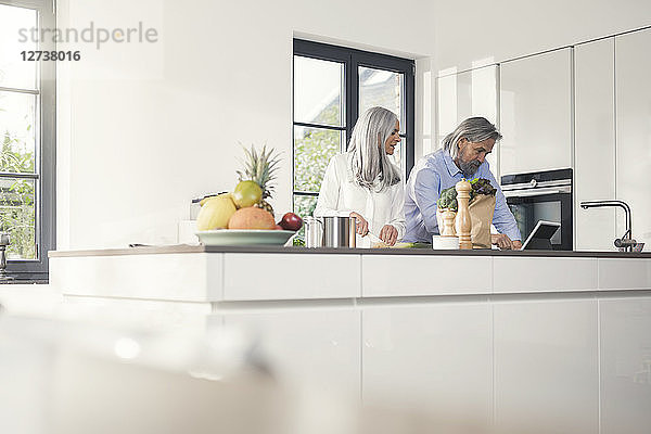 Happy senior couple preparing food in kitchen with online recipe