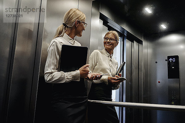 Smiling businesswoman looking in mirror in elevator