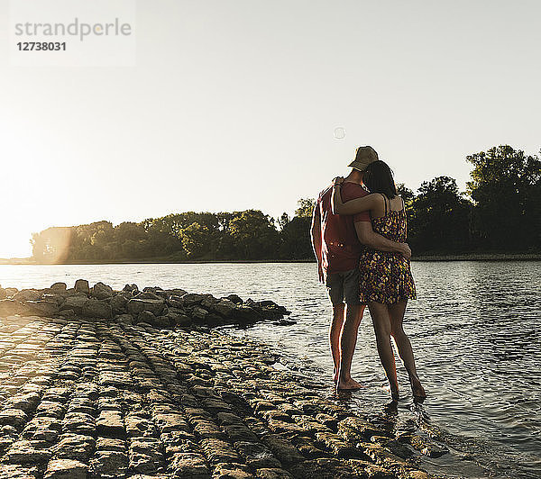 Rear view of young couple embracing at a river at sunset