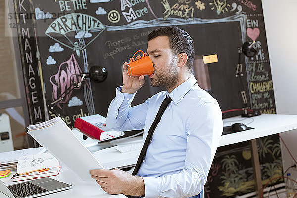Businessman in creative office looking at documents and drinking coffee
