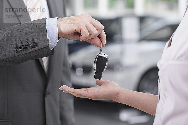 At the car dealer  Salesman handing over car key to client