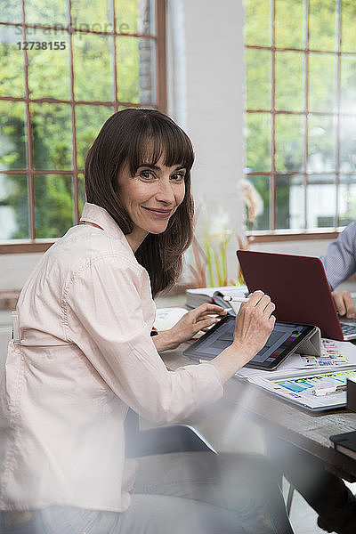 Mature woman sitting in home office  using digital tablet