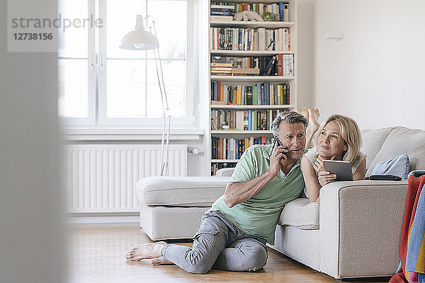 Mature couple at home using cell phone and tablet