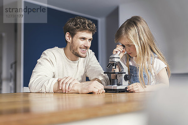 Father watching daughter use a microscope  smiling proudly