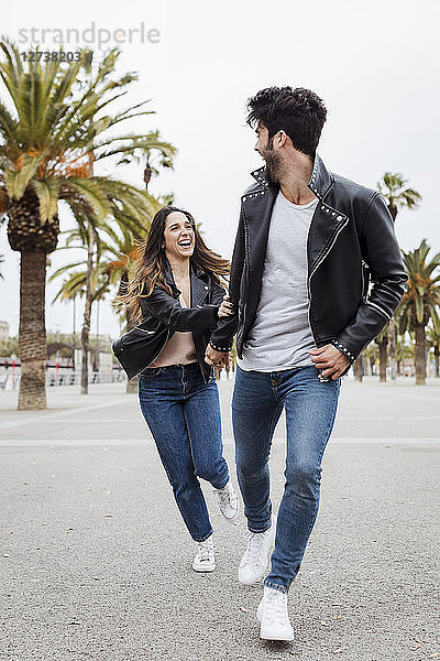 Spain  Barcelona  happy young couple running on promenade with palms