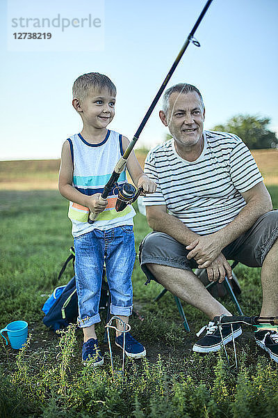 Grandfather and grandson fishing together at lakeshore