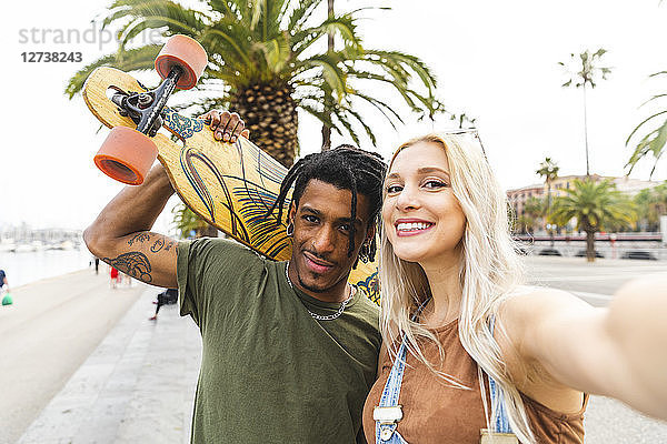 Spain  Barcelona  portrait of multicultural young couple taking selfie at promenade