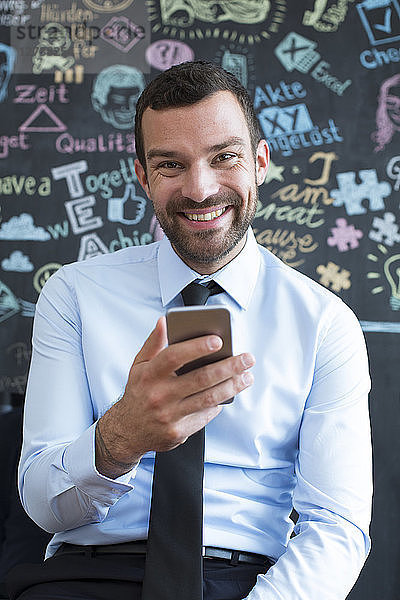Portrait of smiling businessman with cell phone in creative office
