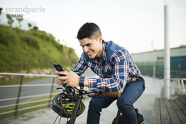 Smiling young man with bicycle looking at smartphone