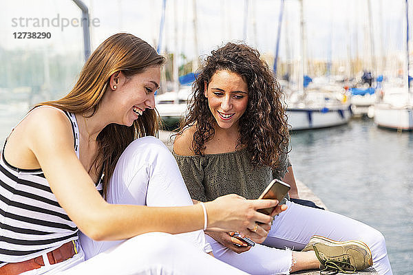 Two happy female friends looking at a smartphone at a marina