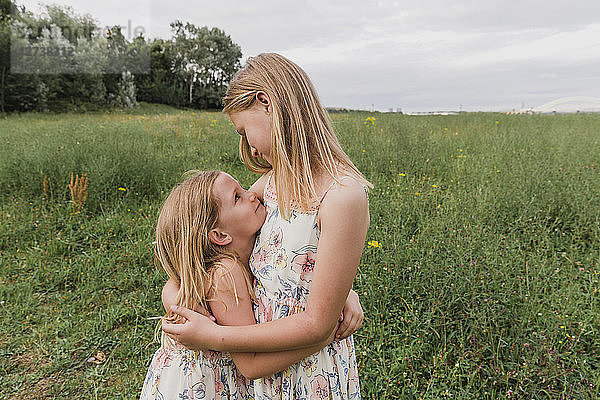 Two little sisters hugging each other on a meadow