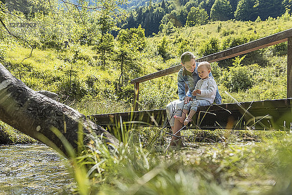Mother and daughter sitting on wooden bridge  mountain stream