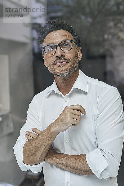 Portrait of man with stubble behind windowpane wearing white shirt and glasses