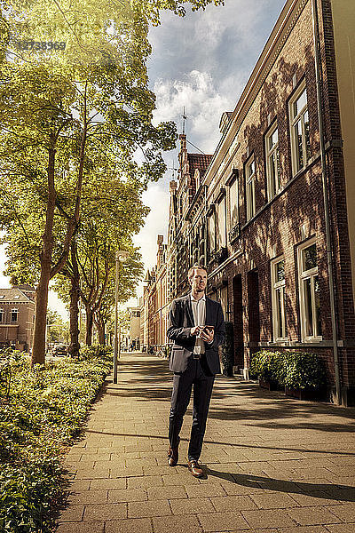 Netherlands  Venlo  businessman with cell phone walking on pavement