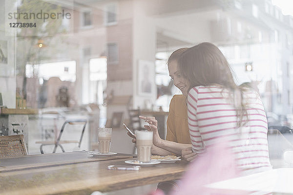 Two girlfriends meeting in a coffee shop  using smartphone