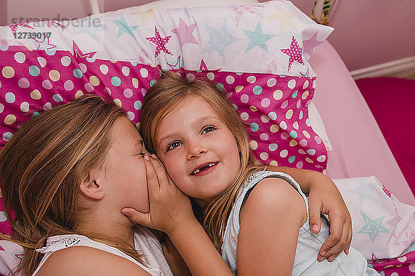 Girl lying on bed with her little sister telling a secret