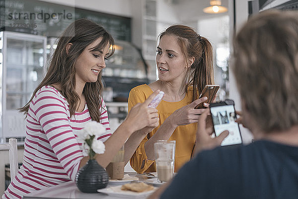 Two girlfriends meeting in a coffee shop  using smartphones