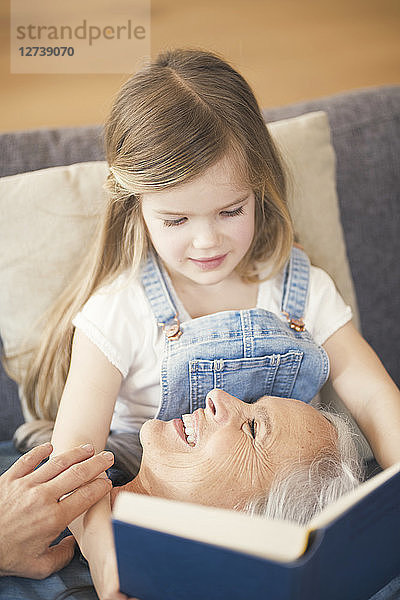 Grandmother and granddaughter sitting on couch  reading together a book