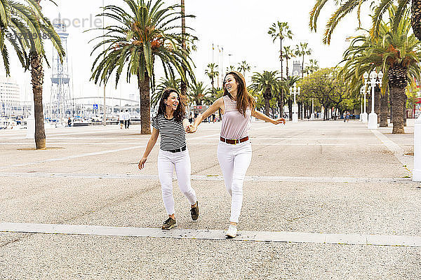 Two happy female friends running on promenade with palms
