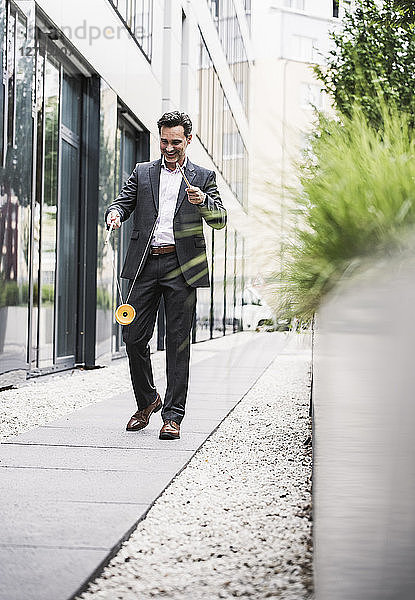 Smiling businessman walking outside office building playing with diabolo