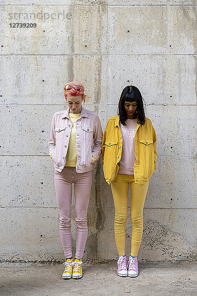 Two alternative friends having fun  wearing yellow and pink jeans clothes  looking down