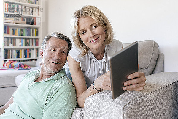 Smiling mature couple at home using tablet