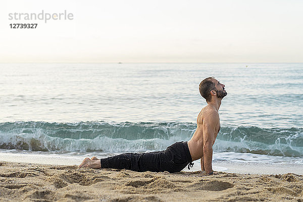 Spain. Man doing yoga on the beach in the evening  cobra pose