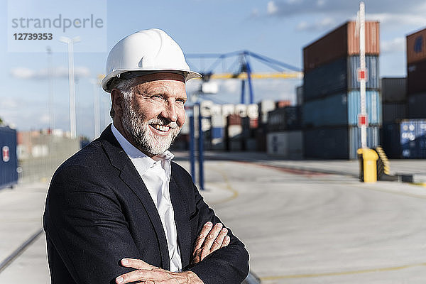 Businessman at cargo harbour  wearing safety helmet  arms crossed