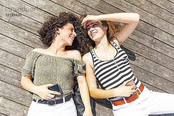 Two happy female friends lying down on a wooden floor