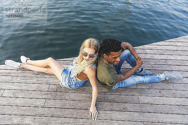 Multicultural young couple relaxing back to back on jetty