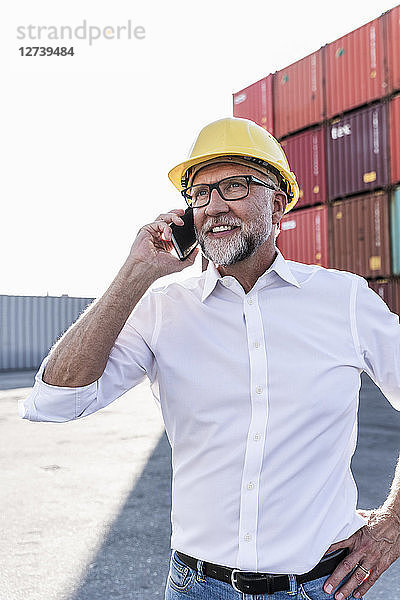 Businessman at cargo harbour  wearing safety helmet  using smartphone