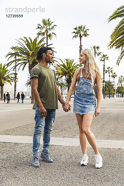 Spain  Barcelona  multicultural young couple standing hand in hand on promenade