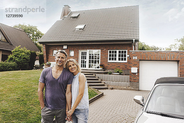 Portrait of smiling mature couple standing in front of their home