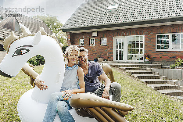 Portrait of smiling mature couple sitting on inflatable pool toy in garden of their home