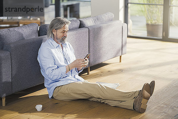 Senior man using smartphone  sitting on floor