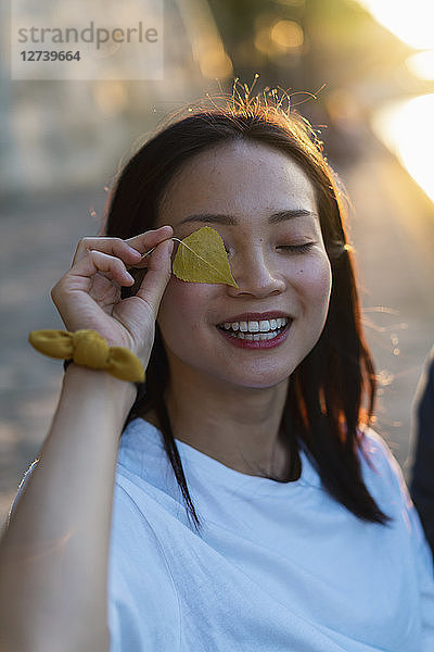 Portrait of happy young woman holding leaf in front of her eye