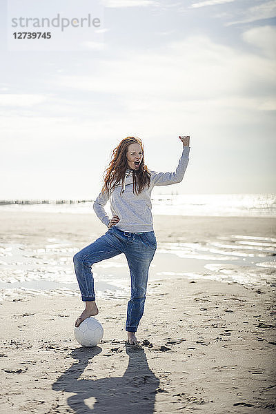 Happy woman having fun at the beach  flexing muscles  playing with soccer ball